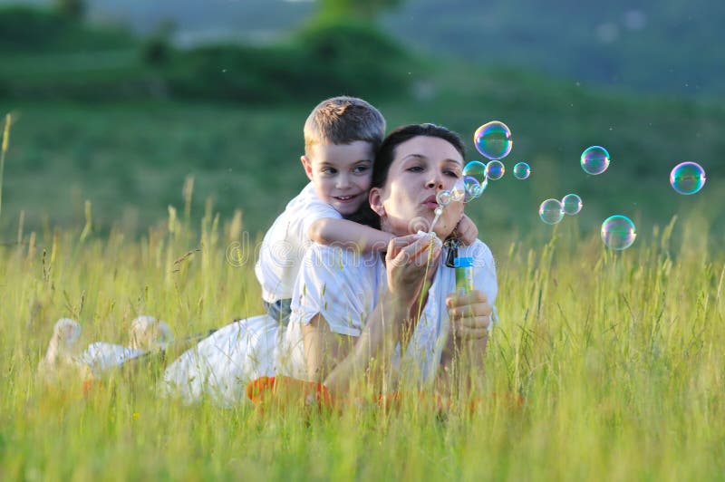 Šťastné dítě a žena venkovní hrát s mýdlové bubliny na louce.