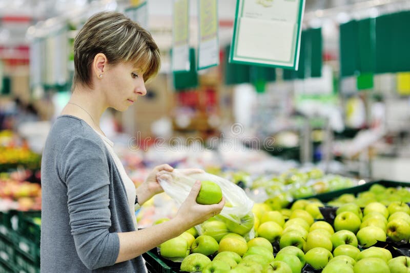 Mujer hermosa selección verde manzana durante compras sobre el verdura.