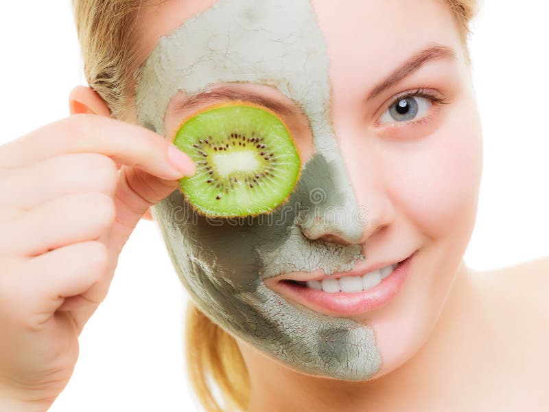 Woman in clay mask on face covering eye with kiwi