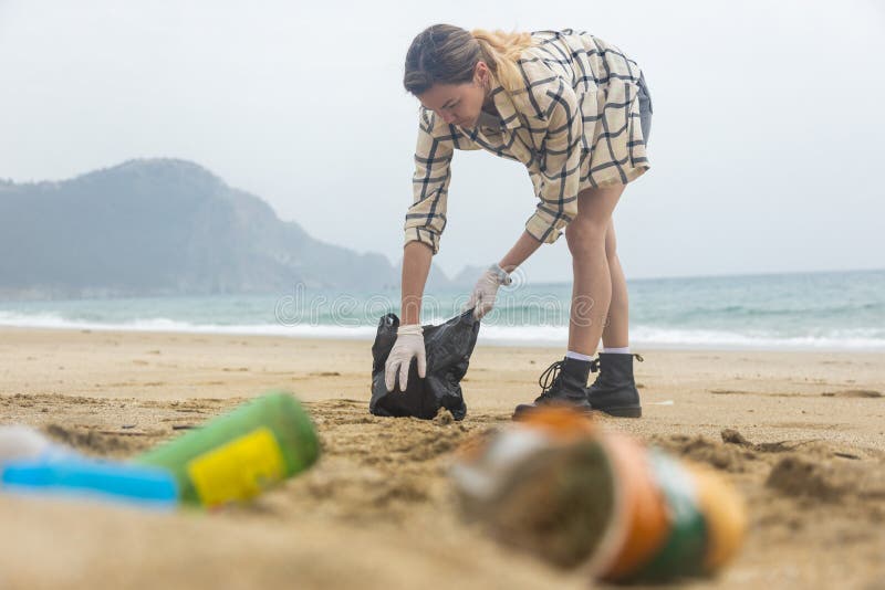 A Woman Cleans Up Trash from the Beach. Plastic Environmental Pollution