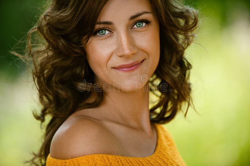 Hermoso mujer joven en naranja un suéter, contra verde de verano.