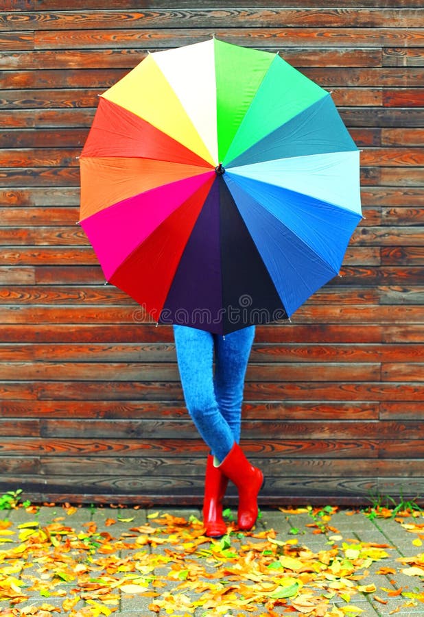 Woman with colorful umbrella wearing a red rubber boots in autumn day over wooden background yellow leafs