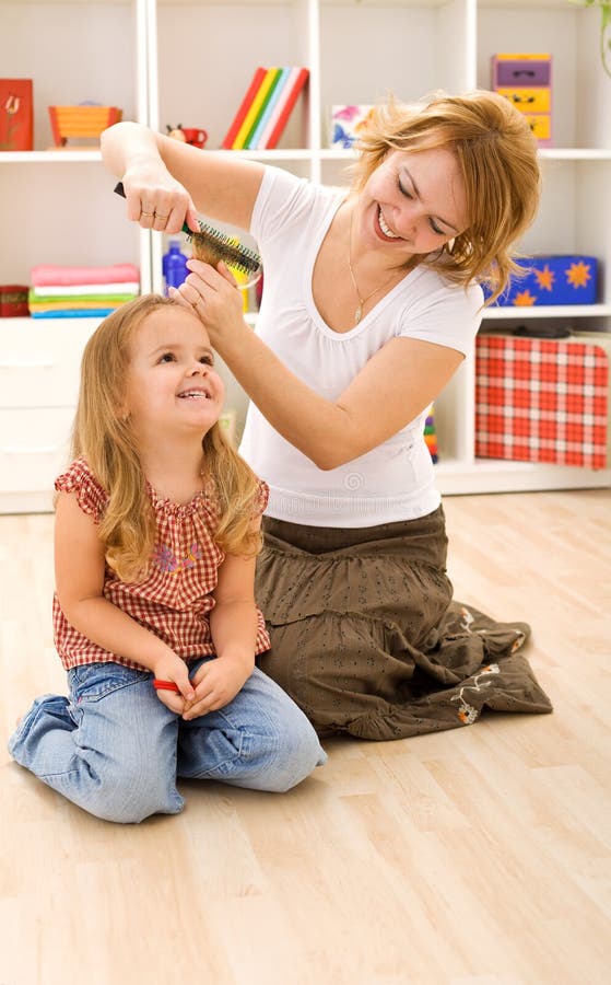 Woman combing little girls hair sitting on the floor in the kids room