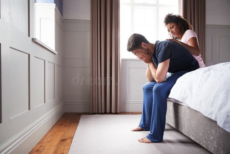 Woman Comforting Man Wearing Pajamas Suffering With Depression Sitting On Bed At Home stock image Woman Comforting Man Wearing Pajamas Suffering With Depression Sitting On Bed At Home stock image