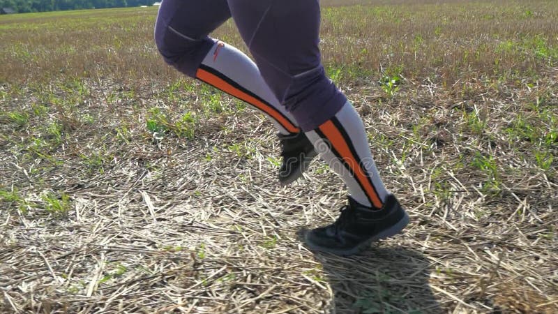 Woman in compression socks run in harvested field. Human legs running in the field.