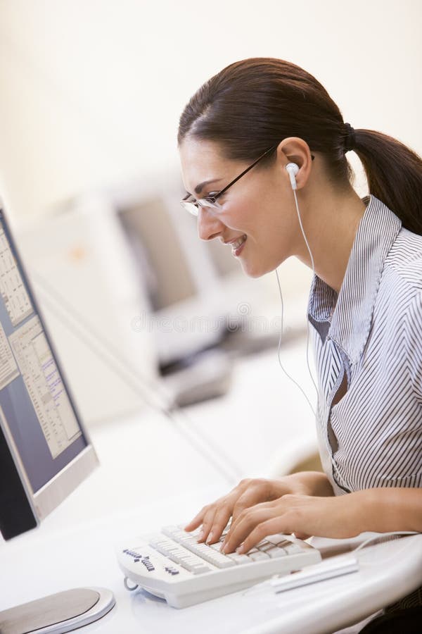 Woman in computer room listening to MP3 Player while typing and smiling
