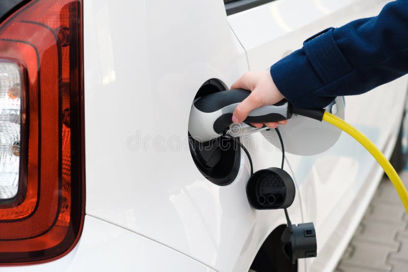 Woman connecting power supply to electric vehicle for charging.