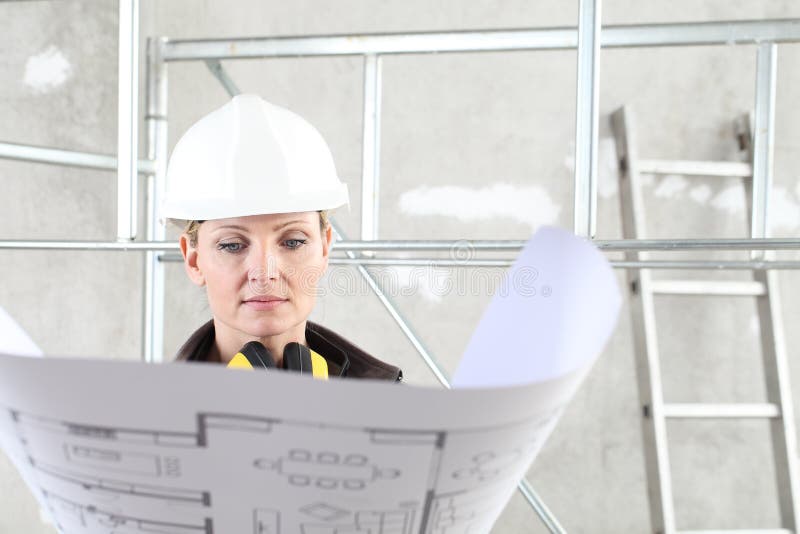 Woman construction worker builder looking at bluprint, wearing helmet and hearing protection headphones in building site indoors stock photos