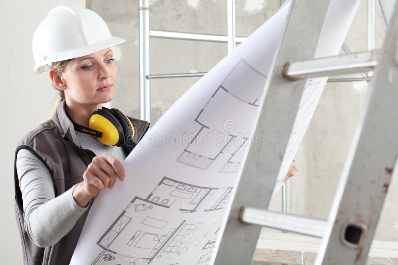 Woman construction worker builder looking at bluprint, wearing helmet and hearing protection headphones in building site indoors royalty free stock photos