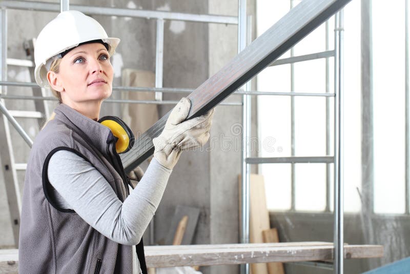 Woman construction worker builder portrait wearing white helmet and hearing protection headphones, holding a metal stud for stock image