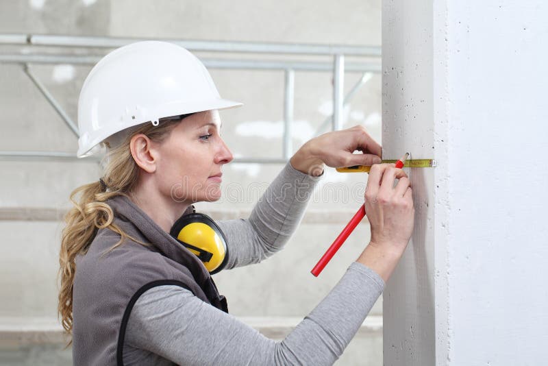 Woman construction worker work with meter tape and pencil, measure wall in interior building site, wearing helmet and hearing stock images