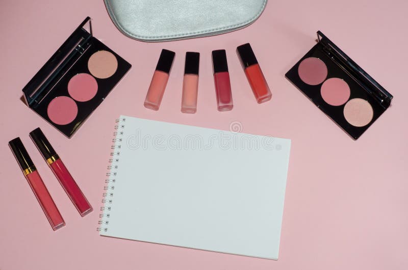Woman cosmetic bag, make up beauty products on pink background, notebook. Red and pink lipstick. Makeup brushes and rouge palettes