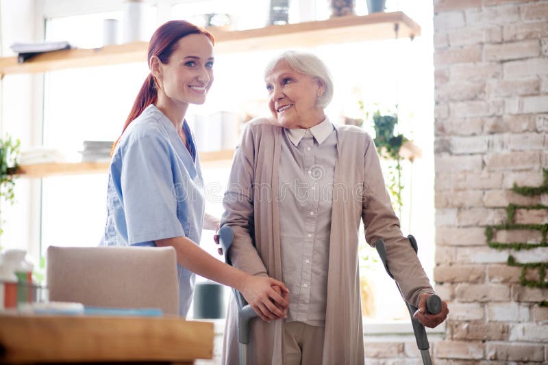 Caregiver Smiling While Helping Aged Woman To Lace Shoes Stock Image Image Of Mature