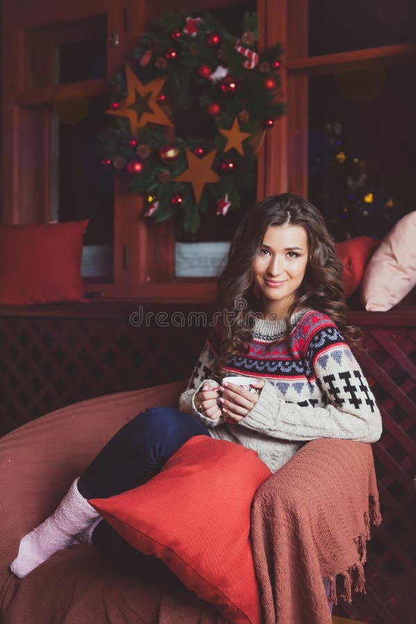 Woman with cup of hot drink sitting on sofa by decorated Christmas tree