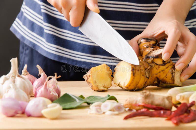 Woman cutting galangal on wooden board for cooking