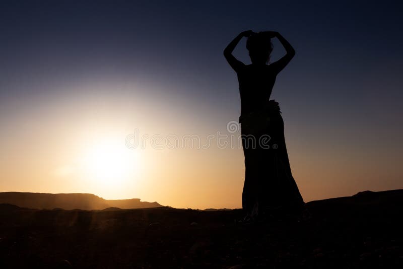 Woman dancing to the famous Arab belly dance. With sunset in the arid desert plain of Namibe. Africa. Angola stock photo Woman dancing to the famous Arab belly dance. With sunset in the arid desert plain of Namibe. Africa. Angola stock photo