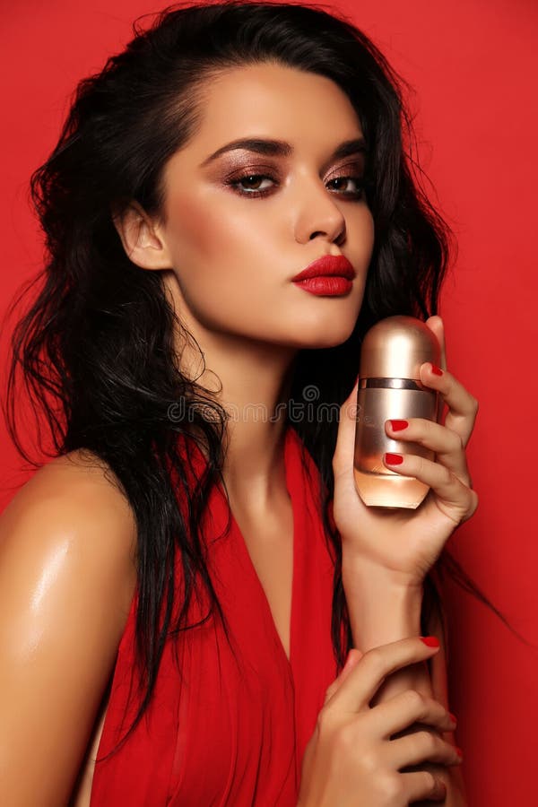 Fashion studio portrait of gorgeous sensual woman with dark hair wears elegant red dress, holding bottle of perfume in hands. Fashion studio portrait of gorgeous sensual woman with dark hair wears elegant red dress, holding bottle of perfume in hands