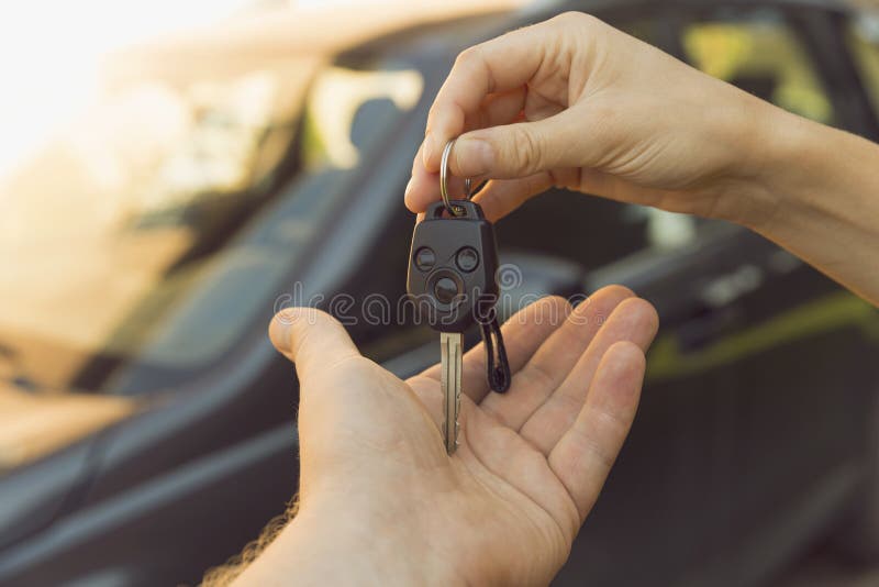 Woman dealer hand giving car keys to man, car on the background in natural light