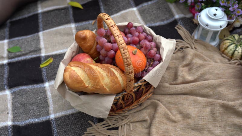 Woman decorates autumn basket with pumpkins, flowers, bread and fruits, autumn picnic still life