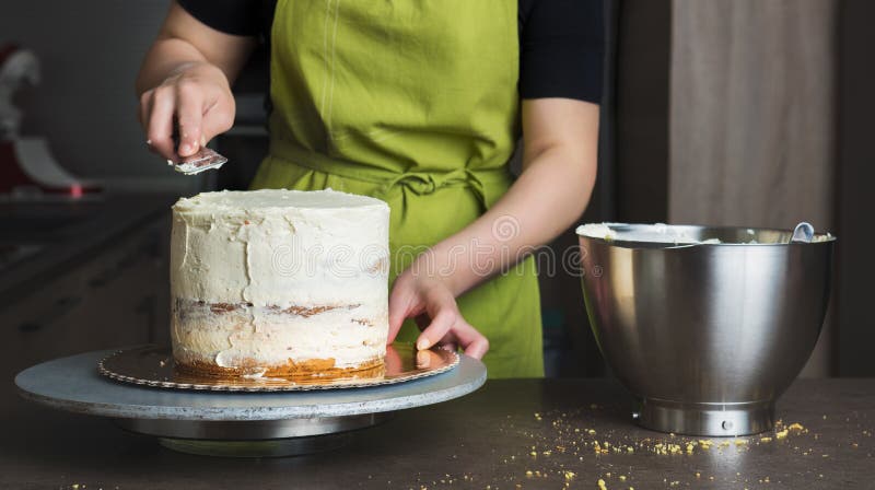 Woman decorating a delicious layered sponge cake with icing cream royalty free stock image