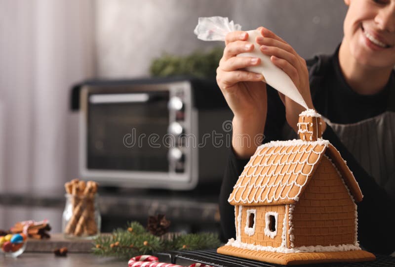 Woman Decorating Gingerbread House with Icing at Table, Closeup Stock
