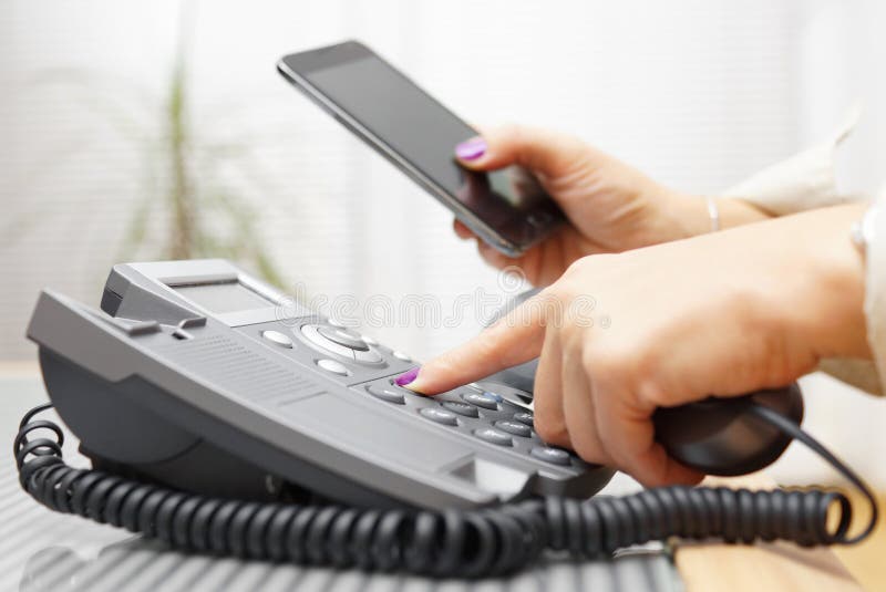 Woman is dialing on land line phone and looking on mobile phone stock photo Woman is dialing on land line phone and looking on mobile phone stock photo