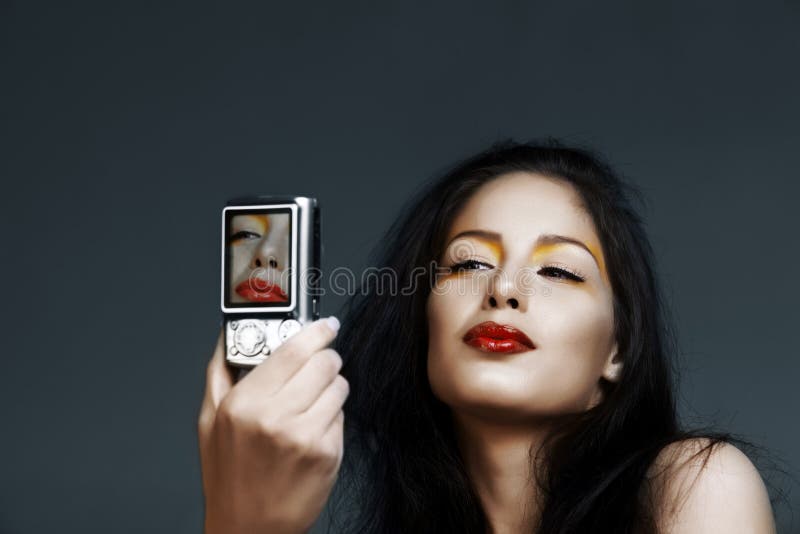 Beautiful brunette woman with modern make-up photographing a self portrait with a digital camera. Beautiful brunette woman with modern make-up photographing a self portrait with a digital camera