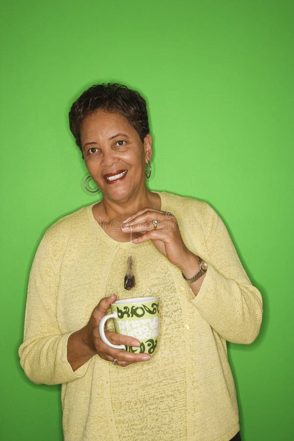 African American female mature adult dipping tea bag in mug. African American female mature adult dipping tea bag in mug.