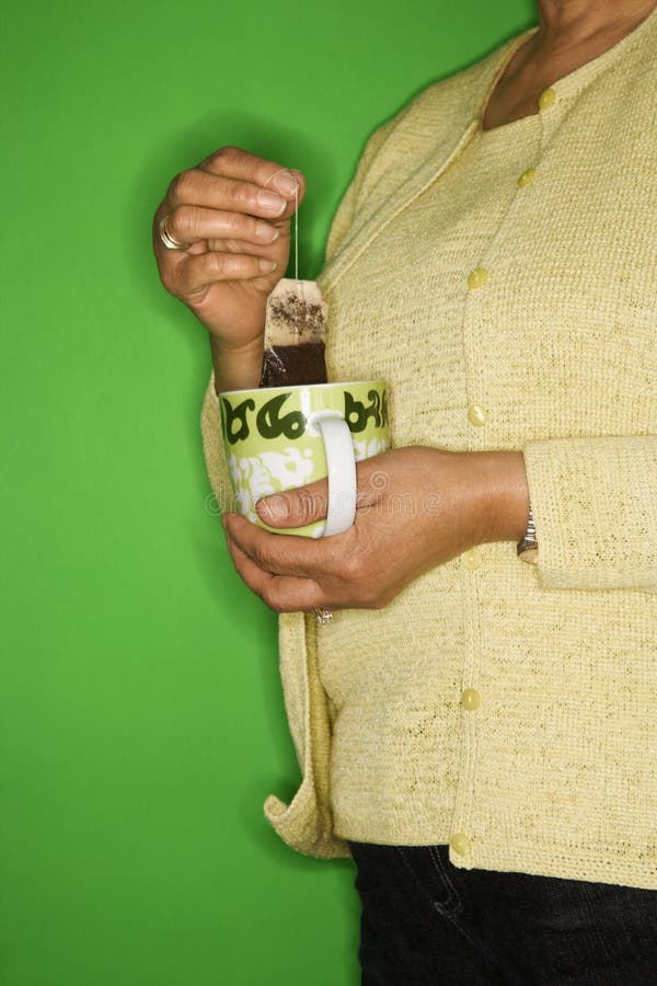 African American female mature adult dipping tea bag in mug. African American female mature adult dipping tea bag in mug.