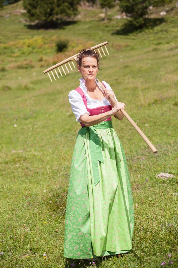 Woman in dirndl in middle age with meadow flower in mouth and ra