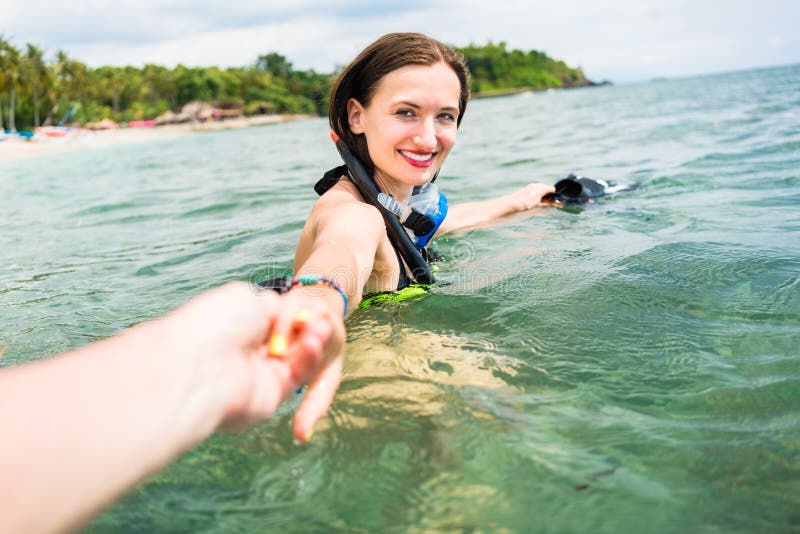 Woman with diving googles dragging partner to the sea