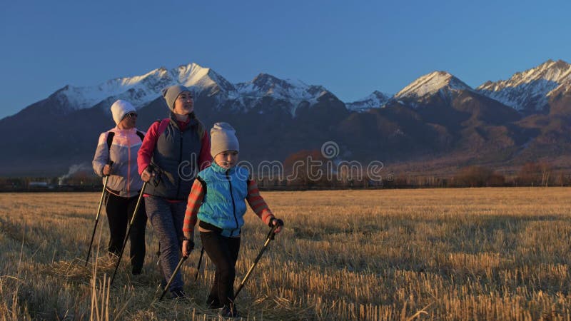 Woman do die Nordic in aard op achtergrond van bergen in gebied lopen Meisjes en kinderen de stokken van de gebruikstrekking en n
