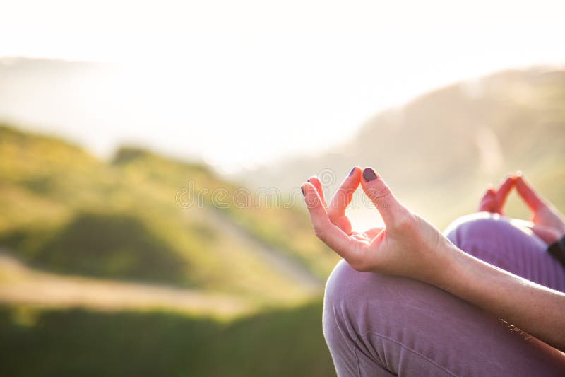 woman doing yoga in beautiful nature background at sunset or sunrise, focus on hand - mindfulness and mental health and hygiene