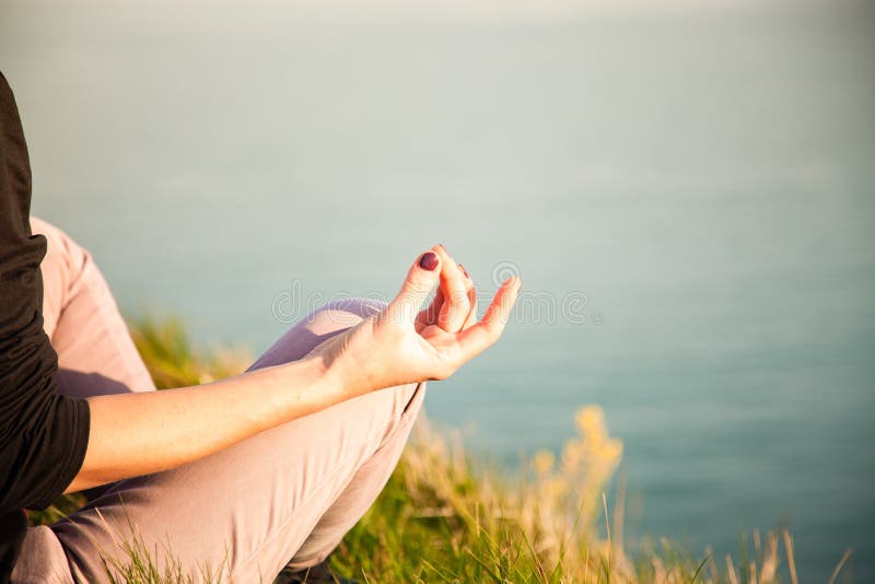 woman doing yoga in beautiful nature background at sunset or sunrise, focus on hand - mindfulness and mental health and hygiene