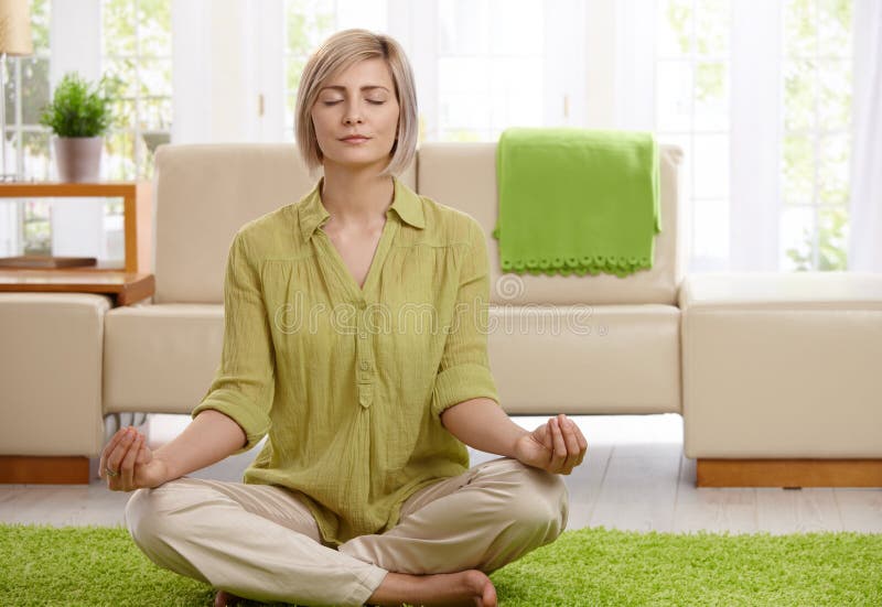 Žena sedí na podlahe doma robiť joga meditácie.