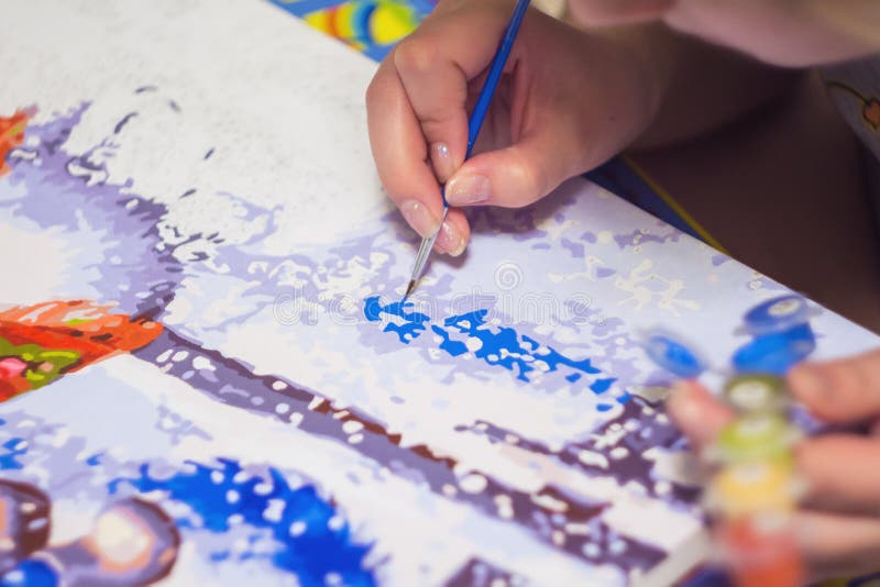 Woman is drawing the paint by numbers by brush with acrylic paint