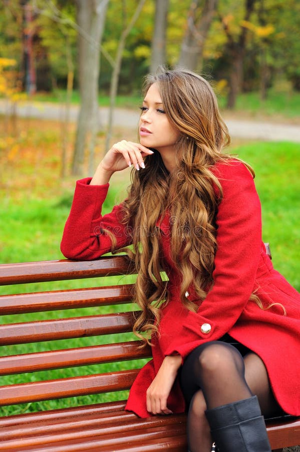 Woman dressed in red coat sitting in autumn park.