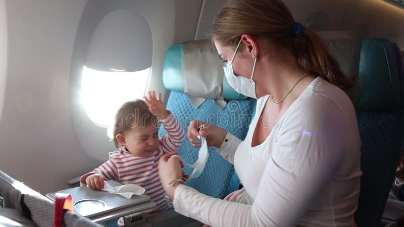 Woman dresses in a protective face gauze bandage on an airplane. Trying to put on a mask on a child. He resists. Protection