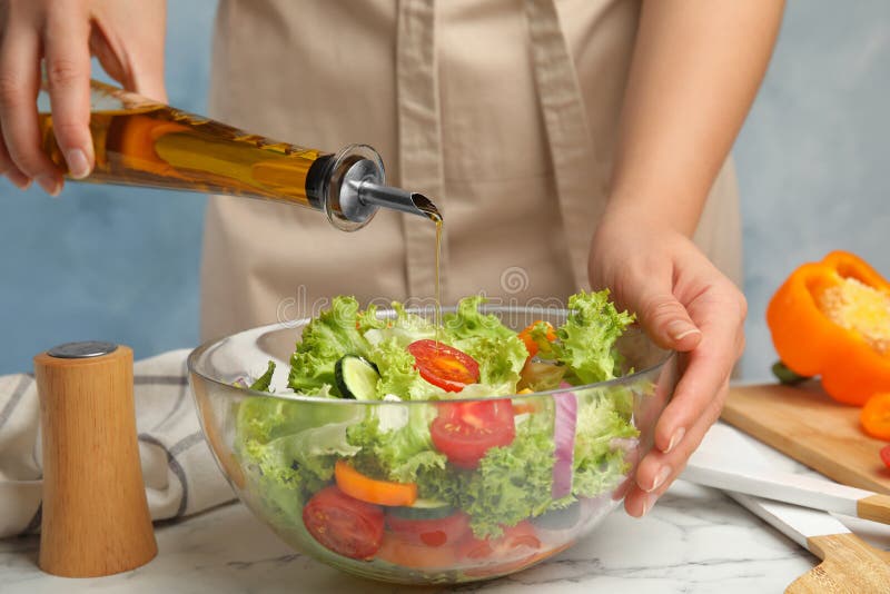 Woman dressing tasty fresh Greek  with olive oil at white marble table, closeup