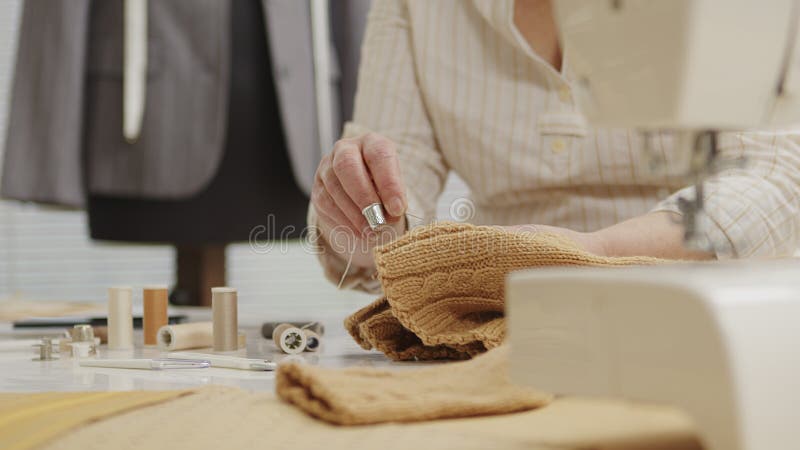 Woman dressmaker working in workshop with tailoring mannequin, sews by hand the sweater. closeup, with tailoring mannequin