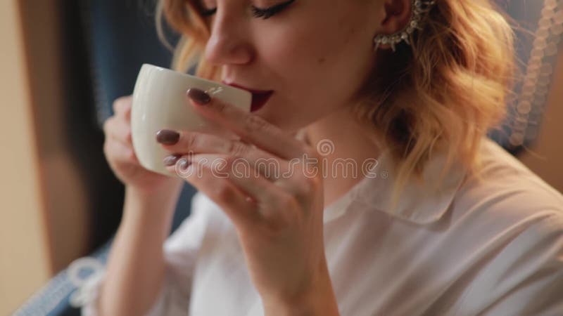 Woman take a cup and drinks tea sitting in a cafe enjoys rest, slowmotion. Hot cafe video