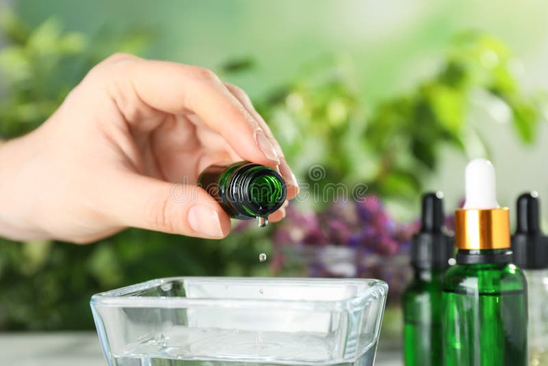 Woman dripping essential oil into bowl on table