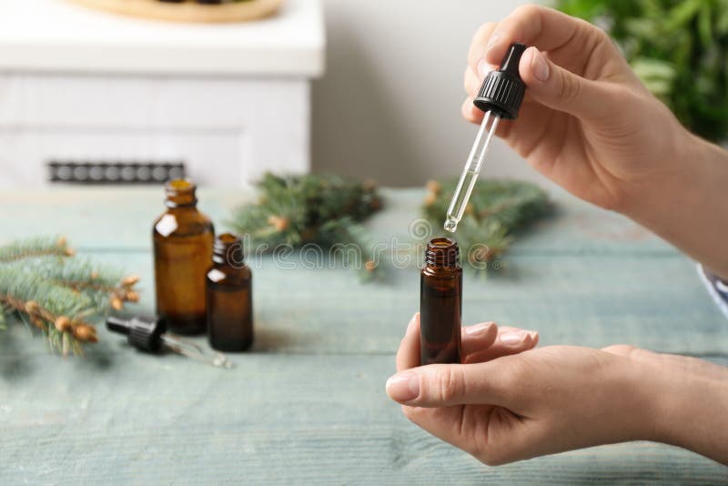 Woman dripping essential oil into glass bottle  at table