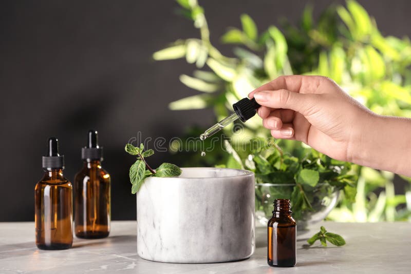 Woman dripping essential oil into mortar with mint on table