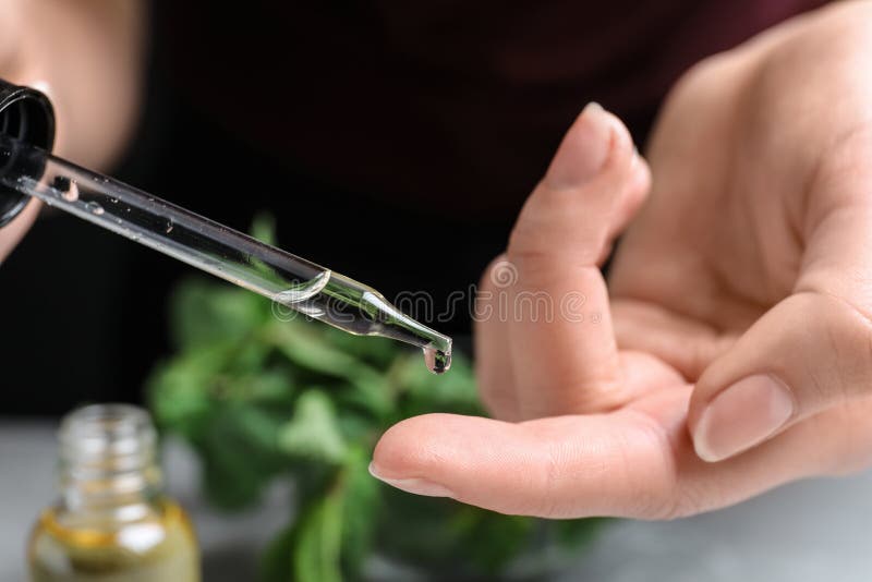 Woman dripping essential oil onto her finger on blurred background