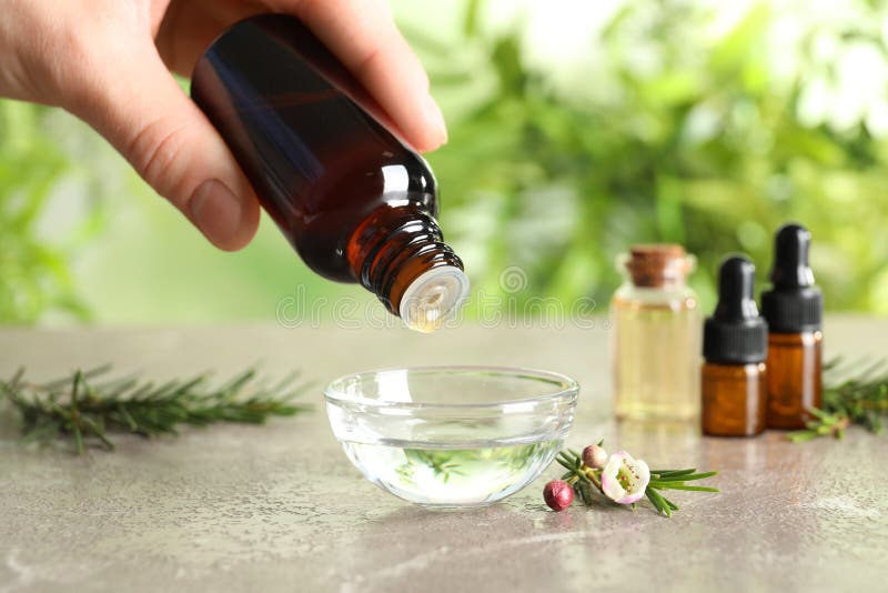 Woman dripping natural tea tree oil in bowl against blurred background