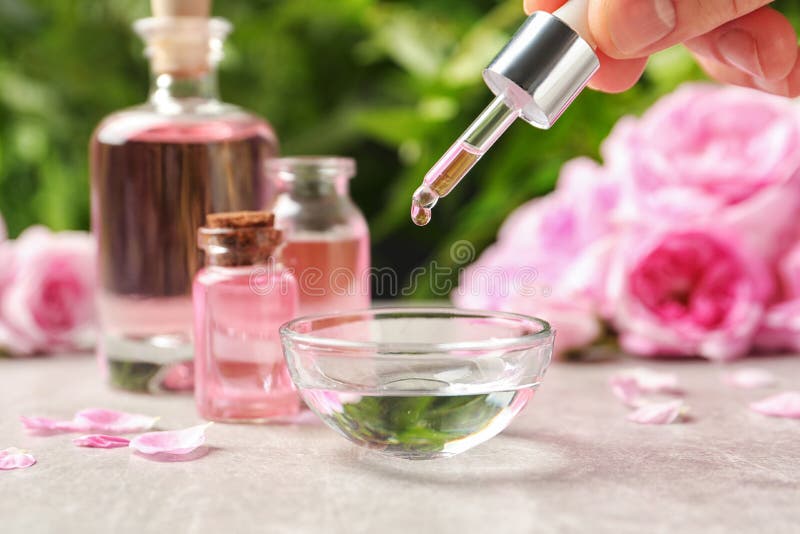 Woman dripping rose essential oil into bowl on table