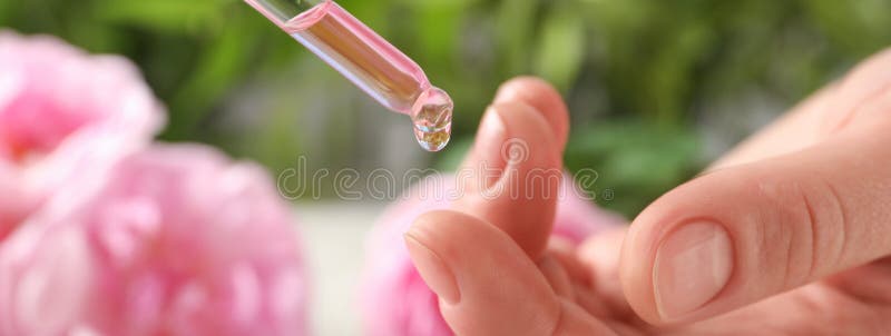 Woman dripping rose essential oil on finger. Banner design