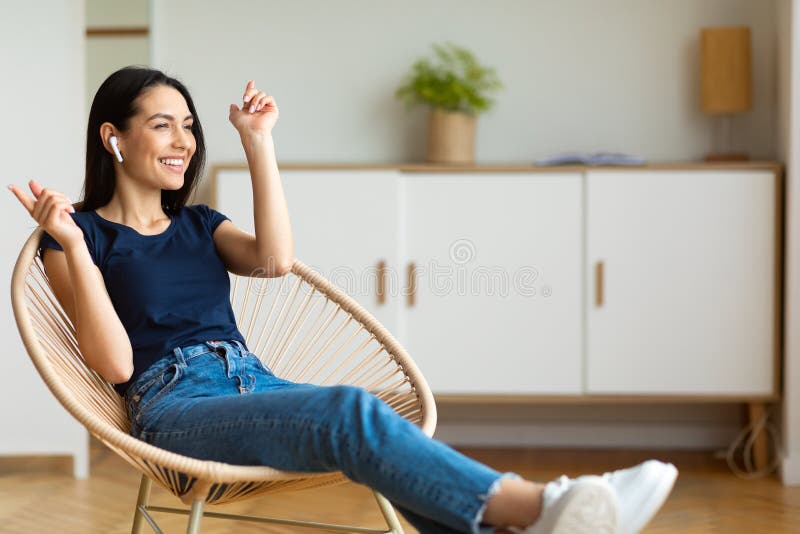 Enjoying Weekend. Happy Woman With Earbuds Enjoying Music Sitting In Modern Chair At Home. Empty Space. Enjoying Weekend. Happy Woman With Earbuds Enjoying Music Sitting In Modern Chair At Home. Empty Space