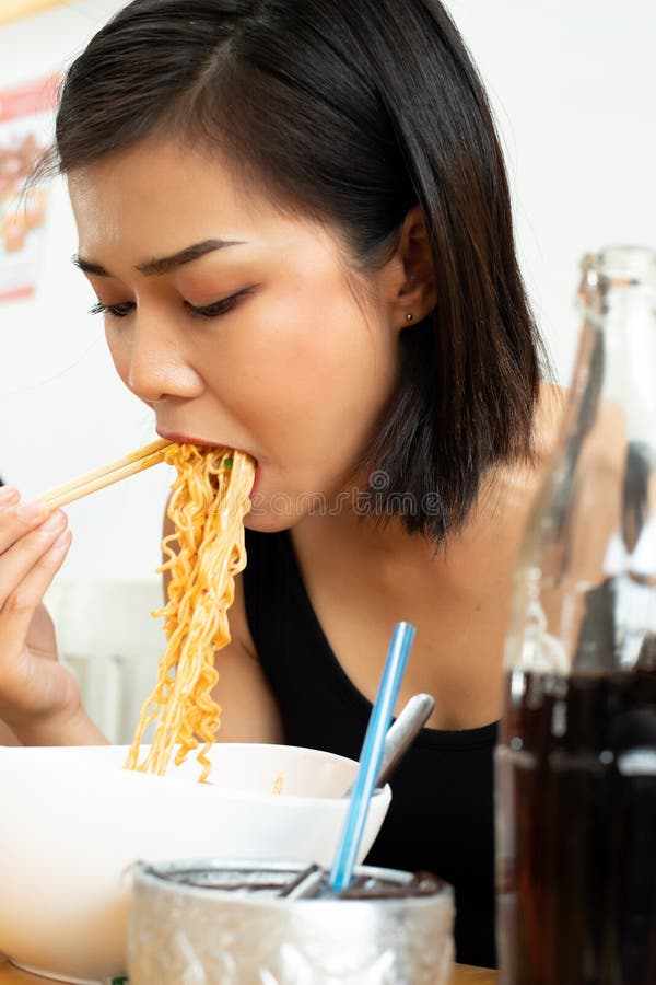 Young Asian Woman eats spicy hot tomyum noodle soup and hanging on chopstick to mouth with sweat delicious enjoy eating